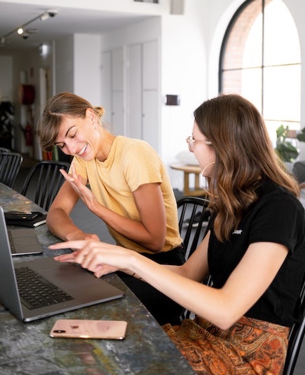 Two girls talking while working on a computer
